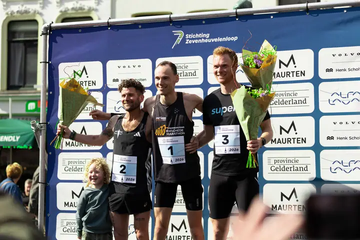 Podium bij de mannen van de Stevensloop 2026, de top drie met bloemen en een kind ernaast