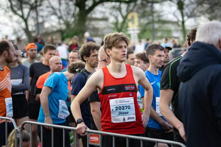 Loper in rood singlet staat geconcentreerd achter het hek te wachten op de start