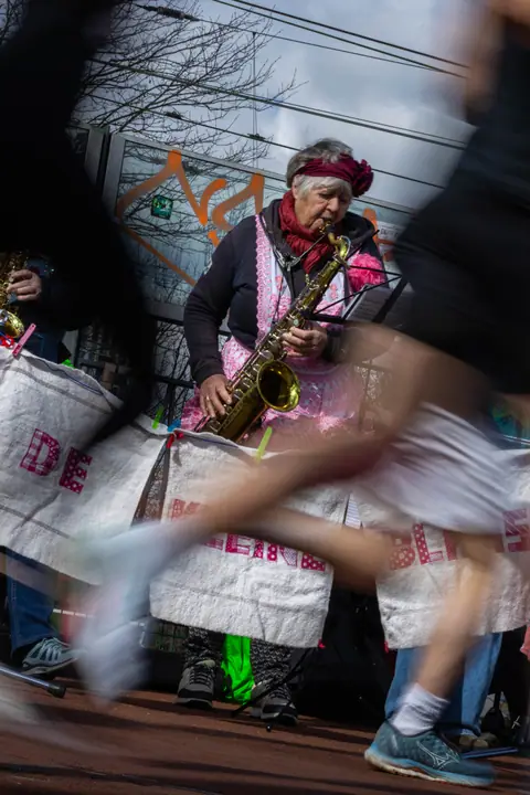 Saxofoniste in roze schort speelt langs de route terwijl een loper voorbij flitst