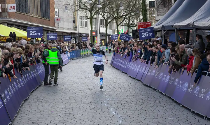 Loper steekt zijn arm in de lucht op de laatste meters, langs rijen publiek in de binnenstad