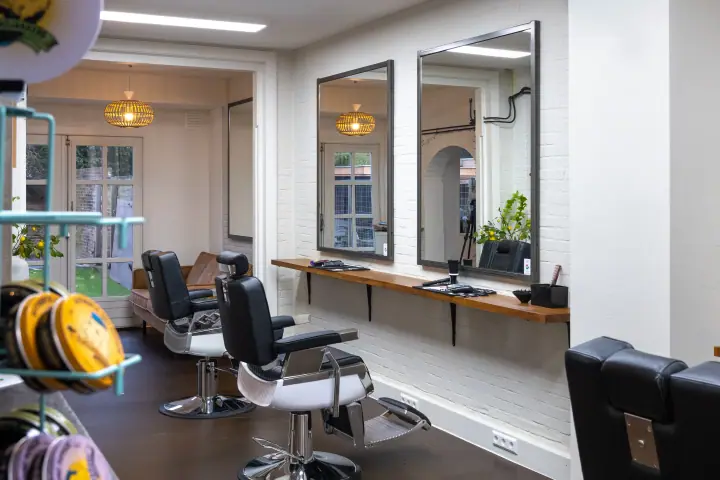 Twee kappersstoelen voor spiegels op witte baksteen, met rieten hanglampen in de achterruimte
