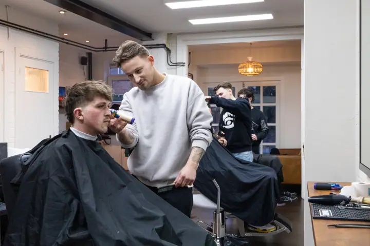 Barbier trimt de snor van een klant terwijl achterin collega's aan het werk zijn