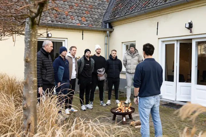 Deelnemers van de Chakana Coaching workshop staan rond een vuurschaal op de binnenplaats van een gele boerderij