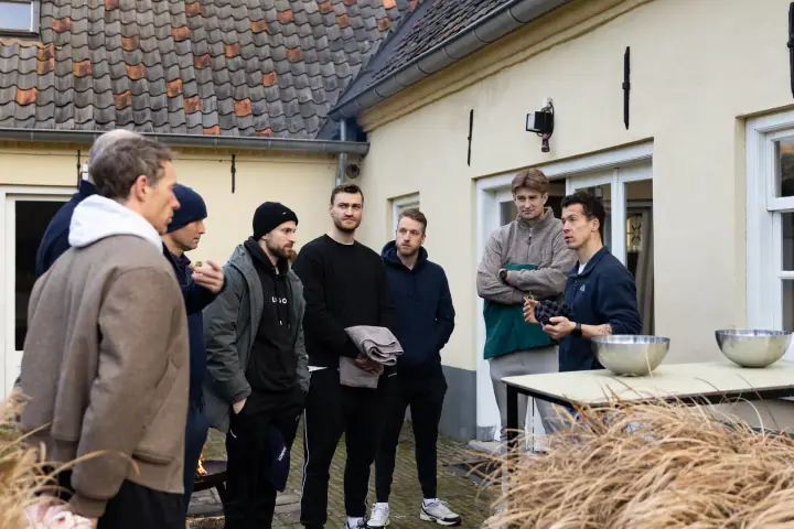 De coach legt de groep iets uit bij een tafel met metalen schalen, vlak voor de ijswateroefening