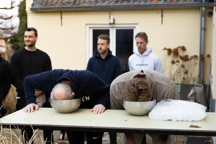Twee deelnemers duwen hun gezicht in een schaal ijswater terwijl de rest van de groep toekijkt