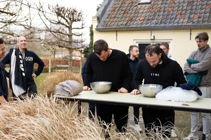 Brede opname van de ijswateroefening in de tuin, met siergras op de voorgrond en kijkende groepsgenoten