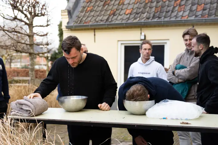 Een deelnemer komt druipend omhoog uit de schaal ijswater, naast hem hangt een ander er nog met zijn gezicht in