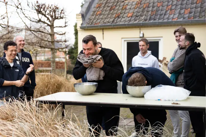 Lachend droogt een deelnemer zijn gezicht af, naast hem hangt een ander nog met zijn hoofd in het ijswater