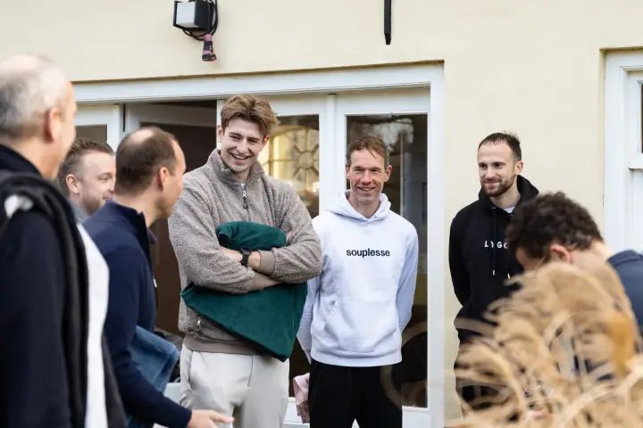 Lachende deelnemers voor de witte tuindeuren, een van hen houdt een groene handdoek tegen zich aan