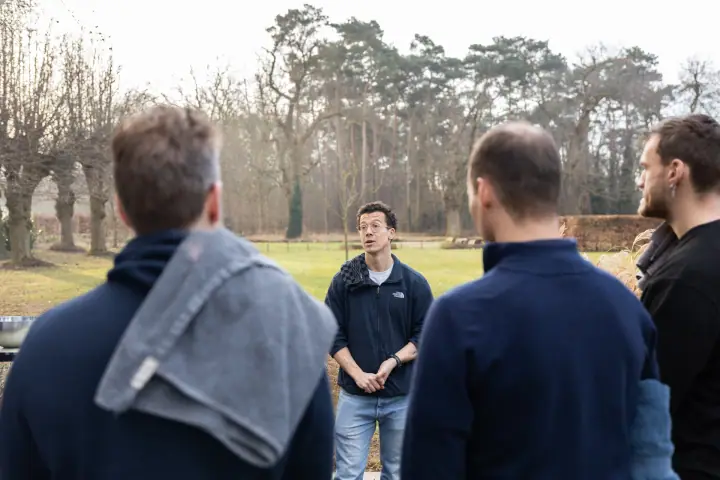 De coach spreekt de groep toe op het gazon, gefotografeerd over de schouders van de luisteraars