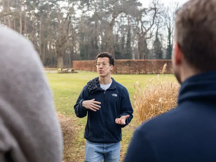 De coach gebaart met beide handen terwijl hij uitleg geeft, tussen twee luisteraars in gefotografeerd