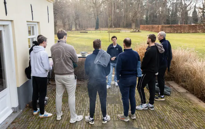 De groep staat op het terras en luistert naar de coach aan de rand van het gazon