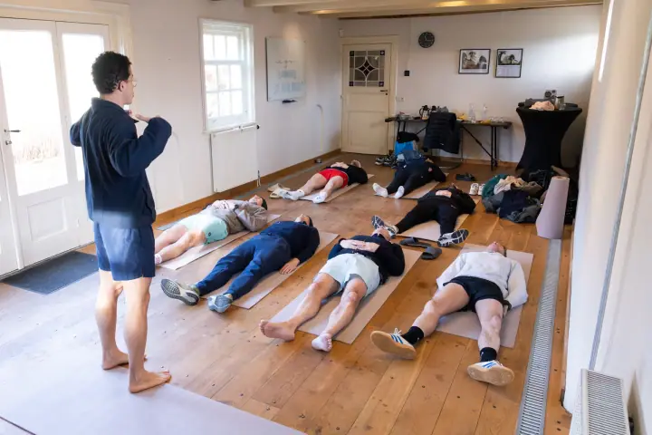 Ademsessie bij Chakana Coaching, de deelnemers liggen op matjes en de coach begeleidt ze op blote voeten