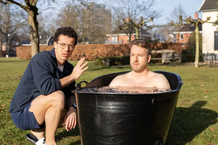 De coach gebaart rustig met zijn hand, de man in het ijsbad kijkt geconcentreerd voor zich uit