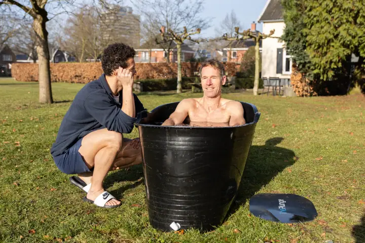 Een glimlach vanuit het ijsbad, terwijl de coach ernaast hurkt en met zijn hoofd in zijn hand luistert