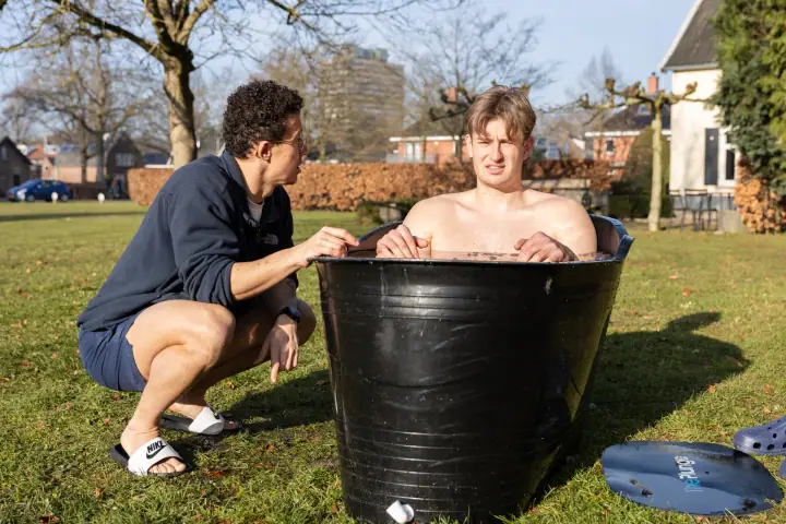 Een jonge deelnemer houdt de rand van het ijsbad vast, de coach moedigt hem van dichtbij aan
