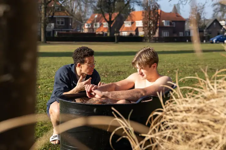Door het droge siergras heen zie je de coach in gesprek met een jonge deelnemer in het ijsbad