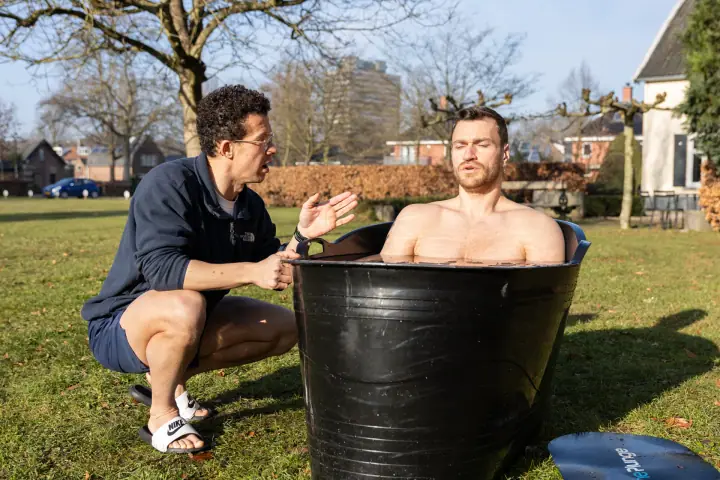 Met gesloten ogen zit een deelnemer in het koude water terwijl de coach hem instructies geeft