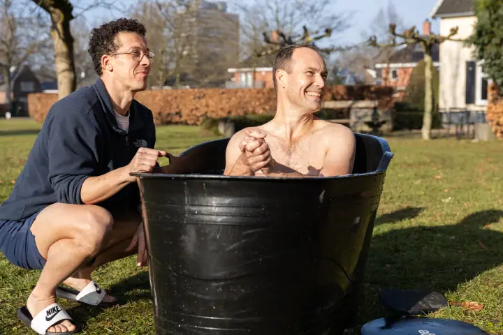 Ontspannen glimlach van een deelnemer in het ijsbad, handen ineen, met de coach aan de rand