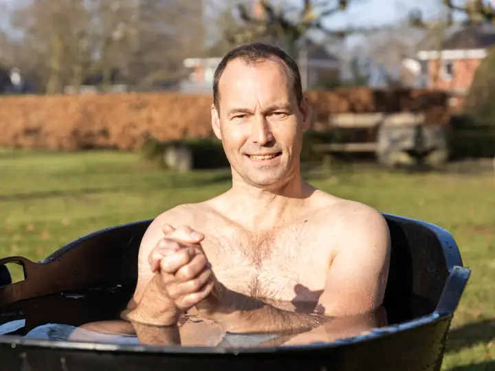 Portret van een deelnemer in het ijsbad die met gevouwen handen tevreden in de camera kijkt