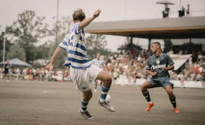 Speler van De Graafschap haalt uit voor een volle tribune terwijl een verdediger van FC Utrecht blokt