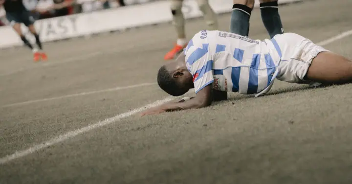 Speler in het blauw-wit van De Graafschap ligt teleurgesteld met zijn gezicht op het gras