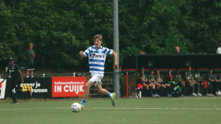 Jeugdspeler van De Graafschap neemt de bal mee over het kunstgras, de grensrechter vlak achter hem