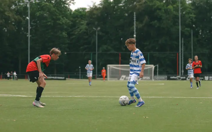 Jeugdspeler van De Graafschap kijkt een NEC-verdediger aan voordat hij de dribbel inzet