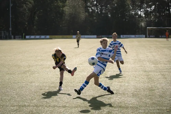 Speler van De Graafschap blokt een schot van een Vitesse-speler in het laag staande zonlicht