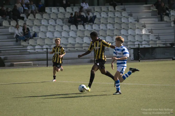 Vitesse-speler stoomt op met de bal voor een halflege tribune, een speler van De Graafschap zit erbovenop