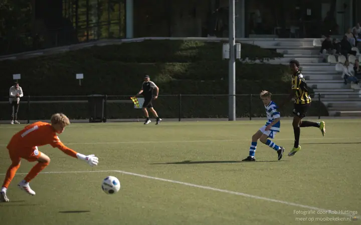 Keeper in oranje komt uit zijn doel naar de bal, een speler van De Graafschap en van Vitesse verderop