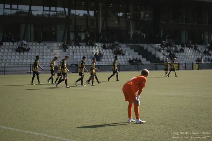 Keeper in oranje staat voorovergebogen terwijl spelers in geel-zwart terug naar hun helft lopen