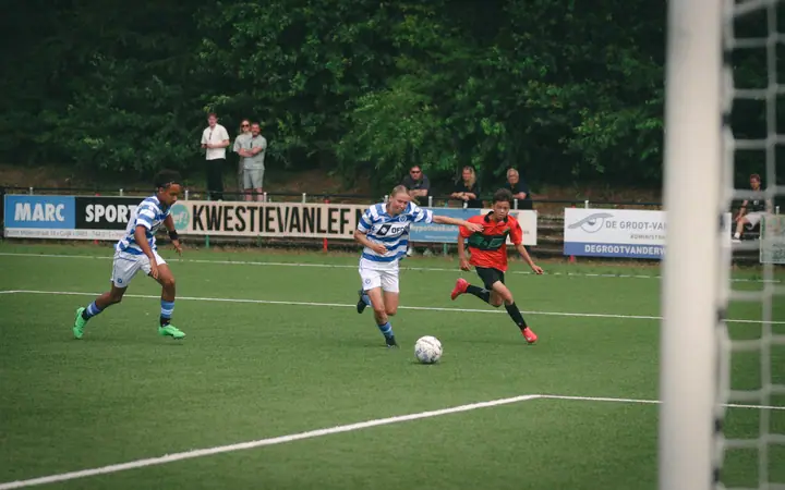 Jeugdspeler van De Graafschap gaat met de bal richting doel, achtervolgd door een speler van NEC