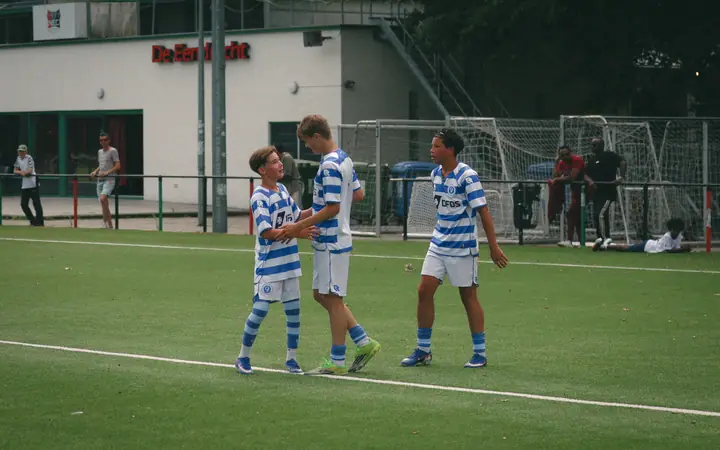 Drie jeugdspelers van De Graafschap feliciteren elkaar met een handdruk voor het clubgebouw