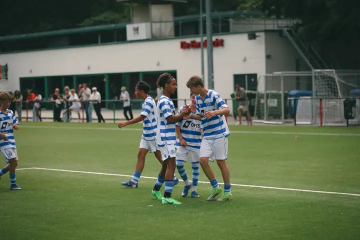 Jeugdspelers van De Graafschap vieren een doelpunt met high fives op het veld