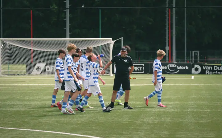 Trainer in het zwart geeft een jeugdspeler van De Graafschap een high five bij het doel