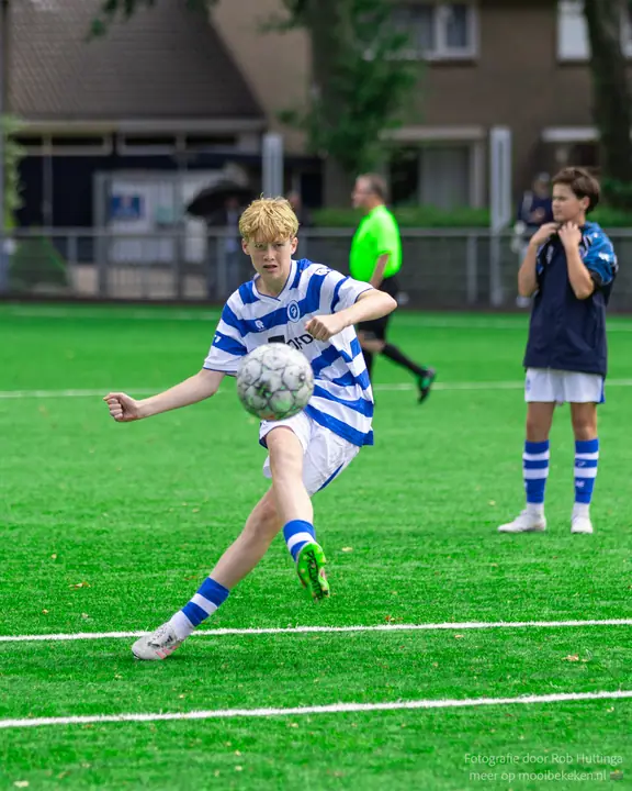 Blonde jeugdspeler van De Graafschap raakt de bal vol op de wreef, een teamgenoot kijkt toe