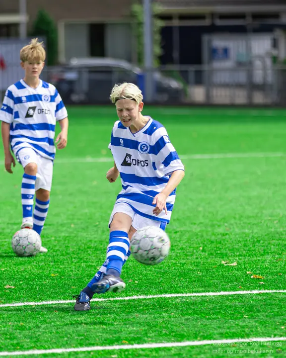 Jeugdspeler van De Graafschap trapt een bal weg tijdens de warming-up, een teamgenoot wacht met de volgende