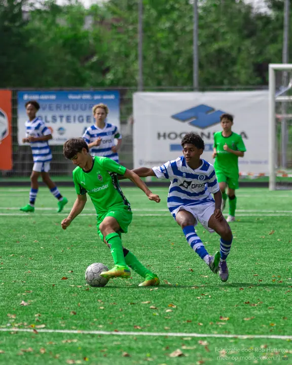 Speler van De Graafschap zet de achtervolging in op een tegenstander in groen die de bal meeneemt
