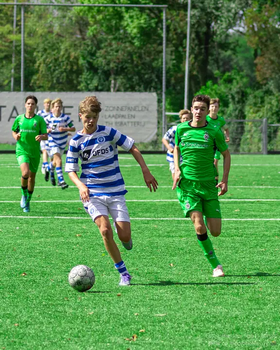 Jeugdspeler van De Graafschap loopt met de bal aan de voet, twee tegenstanders in groen komen eraan