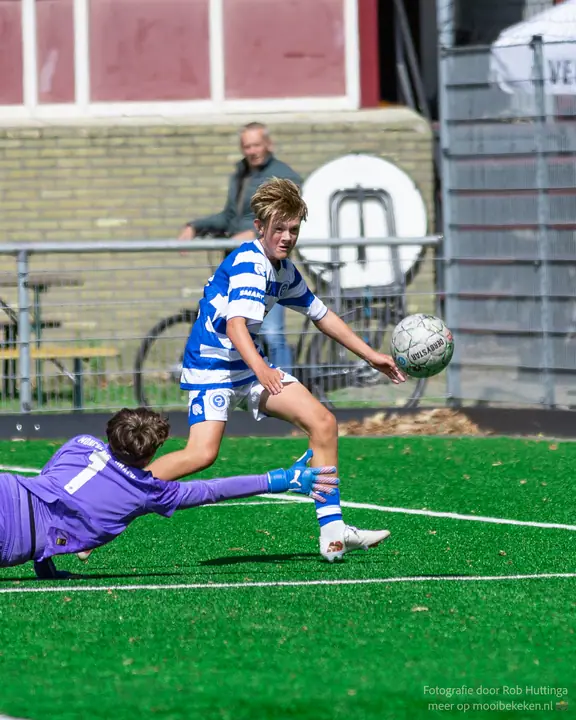 Aanvaller van De Graafschap stift de bal over de duikende keeper in paars