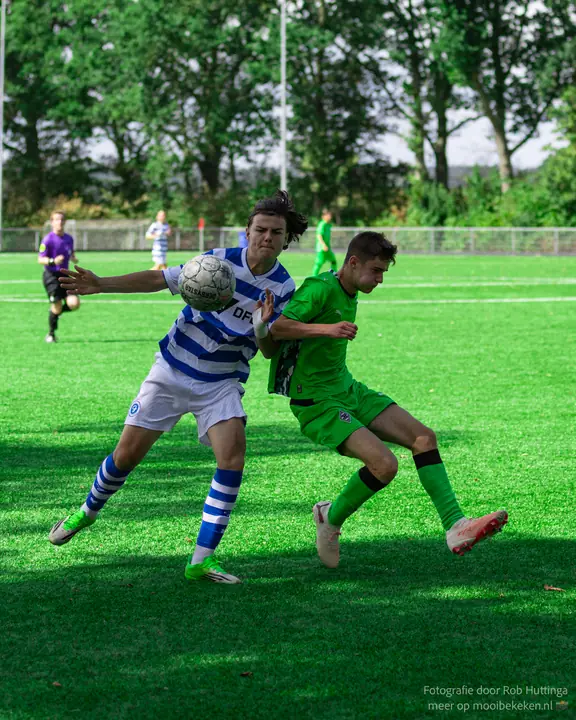 Jeugdspeler van De Graafschap met lang haar vecht om een stuitende bal met een tegenstander in groen