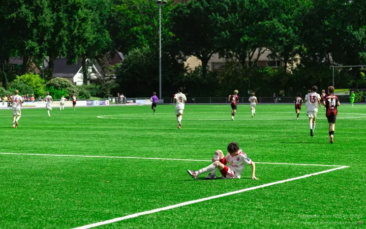Speler in wit-rood tenue zit alleen op het gras terwijl de rest van het veld wegloopt