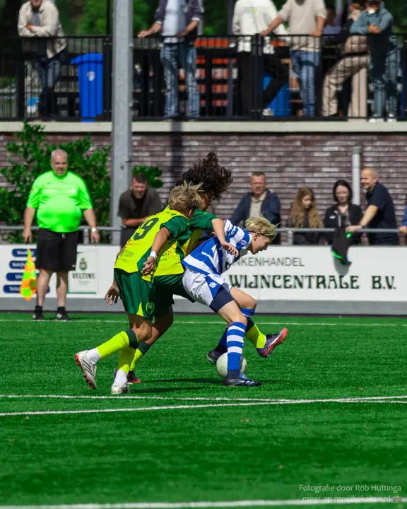 Speler van De Graafschap beschermt de bal tussen twee tegenstanders in geel-groen, scheidsrechter dichtbij