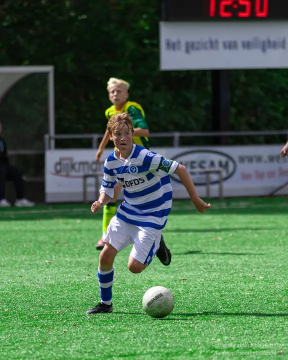 Speler van De Graafschap stuurt de bal vooruit, een tegenstander in geel-groen loopt achter hem