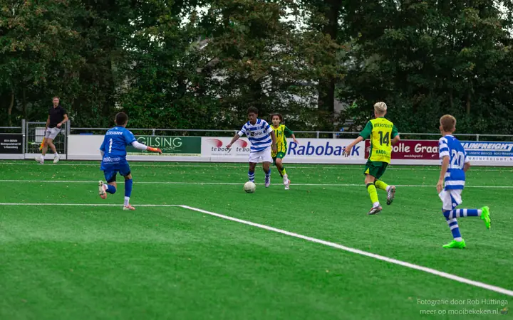 Speler van De Graafschap dribbelt richting de keeper in blauw, tegenstanders in geel-groen haken aan