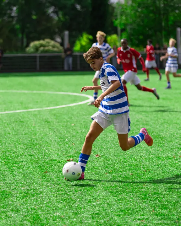 Speler van De Graafschap zet zijn standbeen naast de bal voor een pass, tegenstanders in rood op afstand