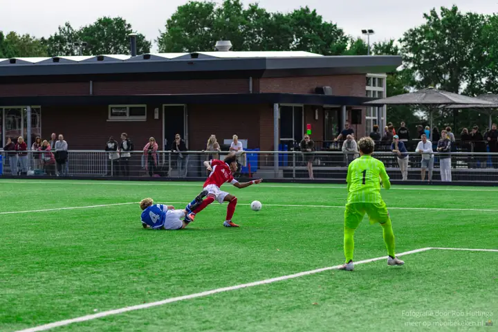 Duel op de grond tussen nummer 4 van De Graafschap en een speler in rood, de keeper kijkt toe