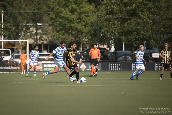 Speler van De Graafschap zit een Vitesse-speler met de bal op de hielen, de scheidsrechter in oranje volgt