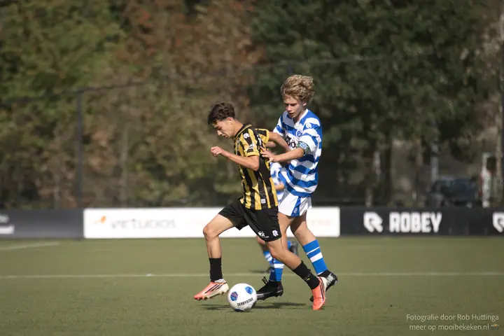 Vitesse-speler neemt de bal aan terwijl een speler van De Graafschap hem van achteren vasthoudt